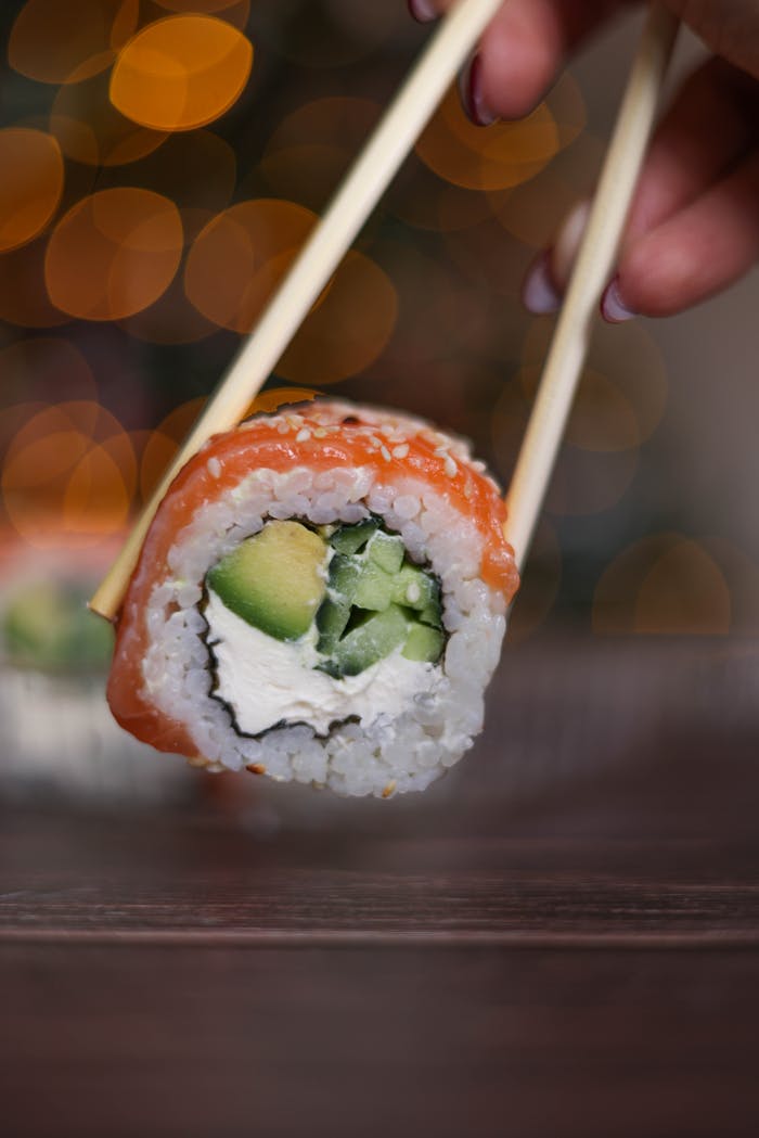 Appetizing sushi roll with salmon, avocado, and rice held by chopsticks.